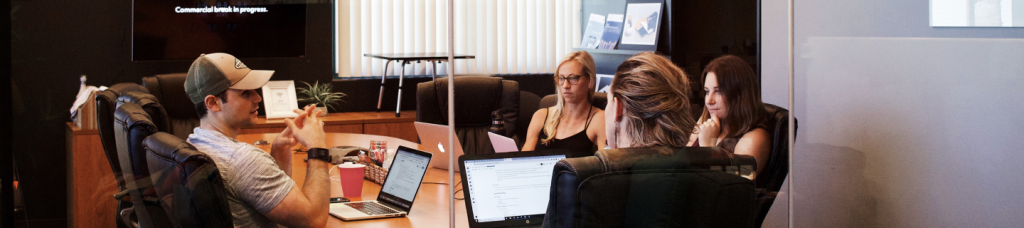 A group of people sitting around laptops on top of a table.